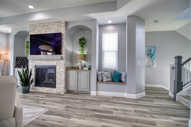 interior space with baseboards, wood finished floors, stairs, a stone fireplace, and recessed lighting