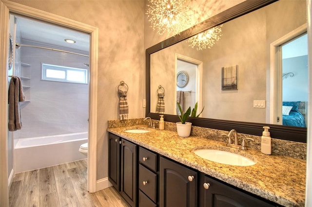 ensuite bathroom featuring double vanity, a sink, toilet, and wood finished floors