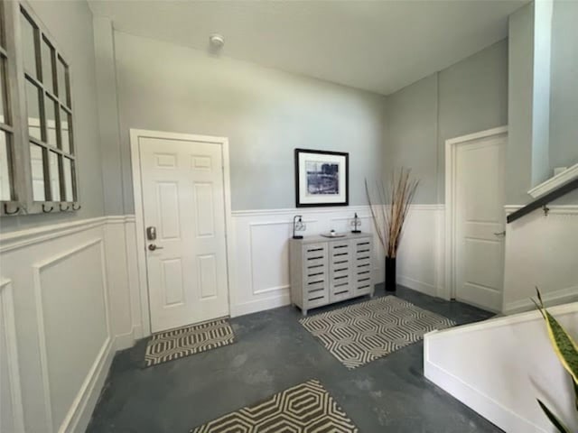 entryway featuring concrete flooring, a wainscoted wall, and a decorative wall