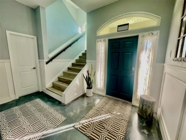 entryway with plenty of natural light, a wainscoted wall, stairs, concrete flooring, and a decorative wall