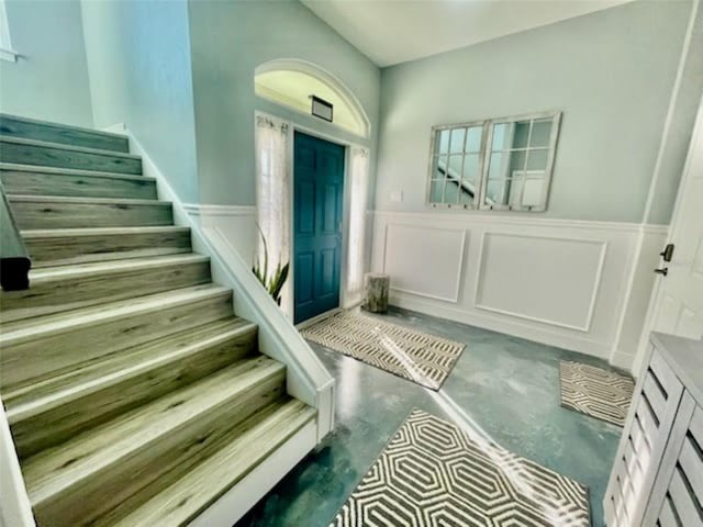 entryway with a wainscoted wall, concrete floors, and stairway