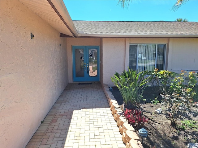 property entrance with a shingled roof, french doors, and stucco siding