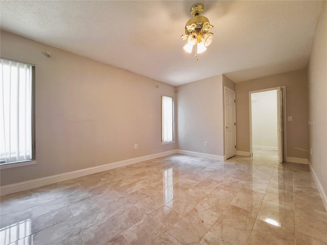 empty room with ceiling fan, a textured ceiling, and baseboards