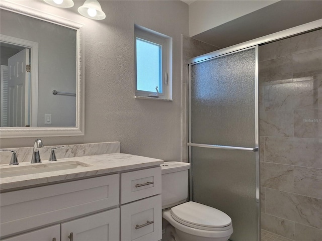 full bathroom featuring toilet, a stall shower, a textured wall, and vanity