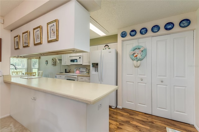 kitchen with kitchen peninsula, white appliances, hardwood / wood-style flooring, and white cabinetry