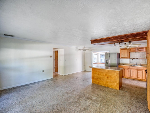 kitchen featuring ceiling fan, stainless steel fridge, sink, a center island, and beam ceiling