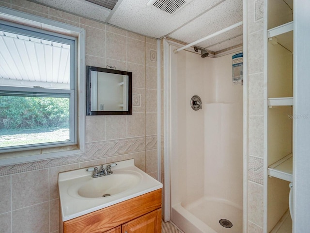 bathroom featuring tile walls, walk in shower, vanity, and a paneled ceiling