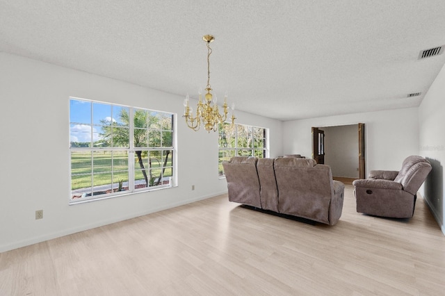 living room featuring light hardwood / wood-style flooring, a notable chandelier, plenty of natural light, and a textured ceiling