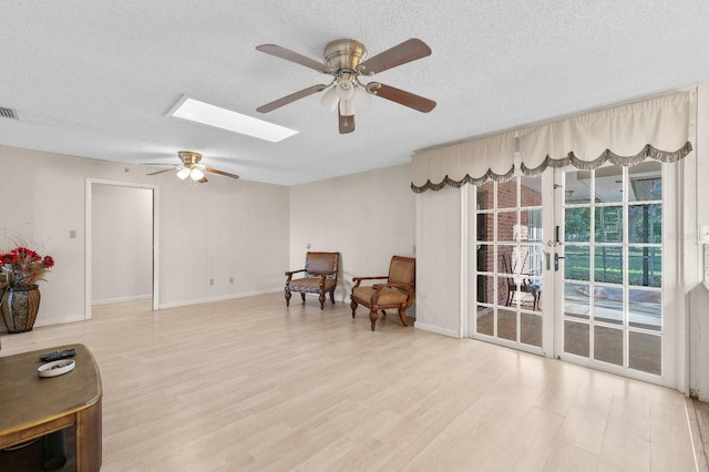 sitting room featuring a textured ceiling, ceiling fan, a skylight, and light hardwood / wood-style flooring