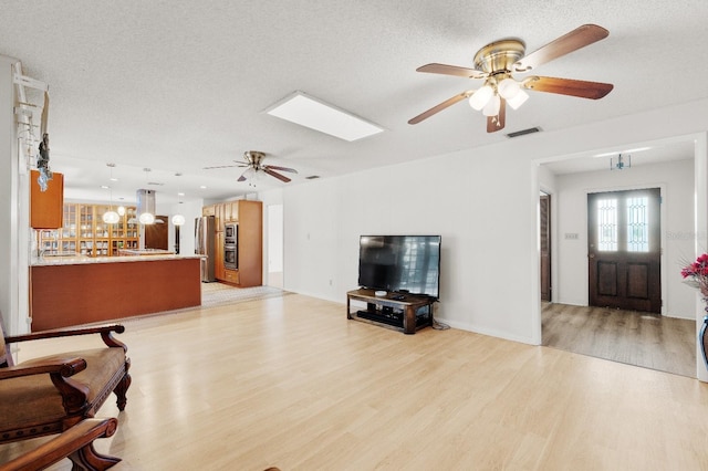 living room with a textured ceiling, ceiling fan, a skylight, and light wood-type flooring