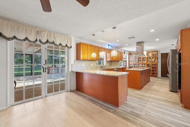 kitchen featuring kitchen peninsula, pendant lighting, tasteful backsplash, french doors, and island exhaust hood