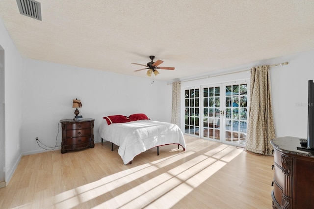 bedroom with ceiling fan, a textured ceiling, light hardwood / wood-style floors, and french doors