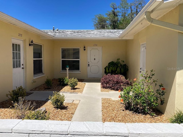 property entrance featuring roof with shingles and stucco siding