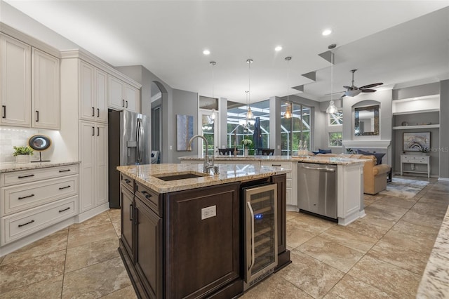 kitchen featuring beverage cooler, light stone counters, decorative light fixtures, a center island with sink, and appliances with stainless steel finishes