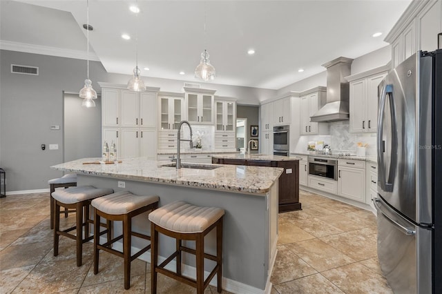 kitchen with appliances with stainless steel finishes, tasteful backsplash, a kitchen island with sink, sink, and wall chimney range hood