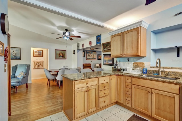 kitchen with ceiling fan, dark stone countertops, light hardwood / wood-style floors, sink, and kitchen peninsula