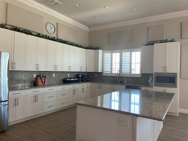 kitchen featuring white cabinets, appliances with stainless steel finishes, a kitchen island, tasteful backsplash, and dark stone counters