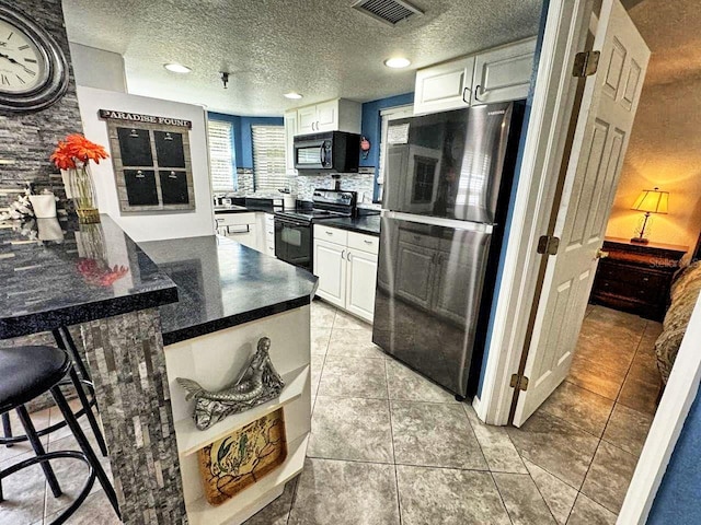 kitchen with light tile floors, a textured ceiling, backsplash, white cabinetry, and black appliances