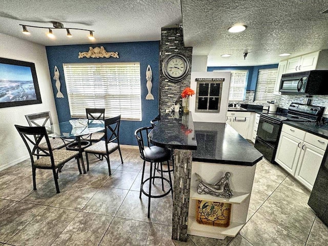 kitchen with light tile floors, a textured ceiling, white cabinetry, black appliances, and track lighting