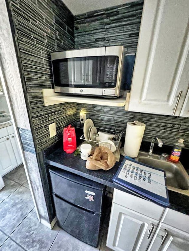 kitchen featuring sink, tasteful backsplash, white cabinetry, and light tile floors