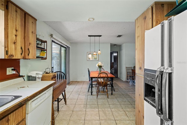 kitchen featuring hanging light fixtures, tile counters, stainless steel refrigerator with ice dispenser, white dishwasher, and a textured ceiling