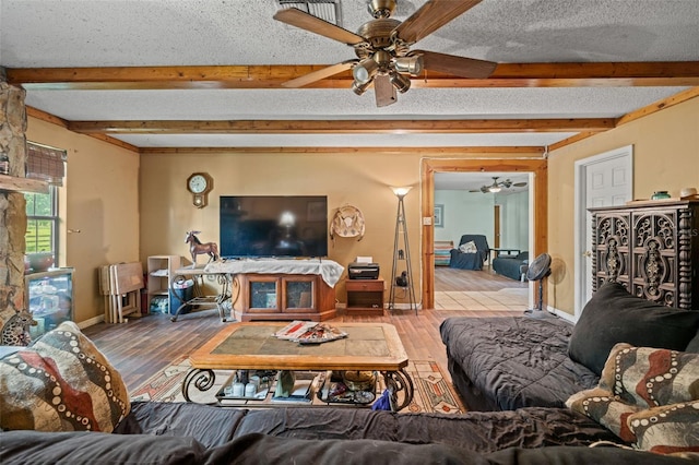 living room with beamed ceiling, ceiling fan, and a textured ceiling