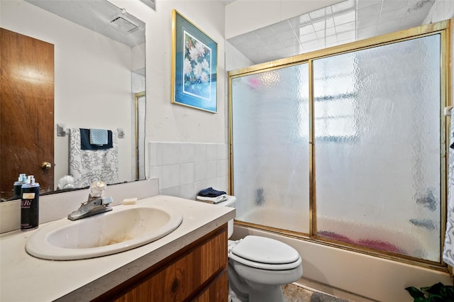 full bathroom with tile walls, enclosed tub / shower combo, toilet, and vanity