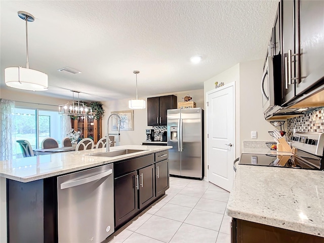 kitchen with appliances with stainless steel finishes, sink, backsplash, an island with sink, and pendant lighting