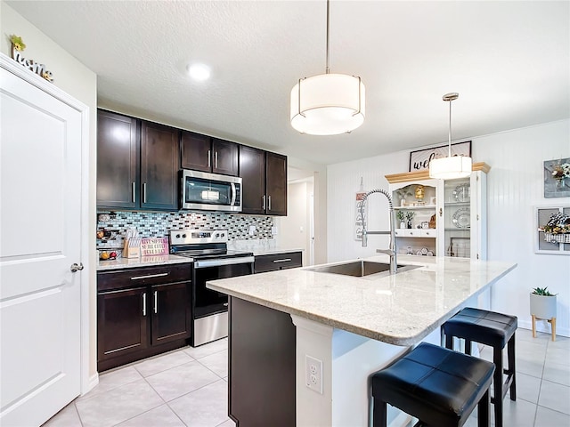 kitchen featuring backsplash, stainless steel appliances, a kitchen island with sink, sink, and pendant lighting