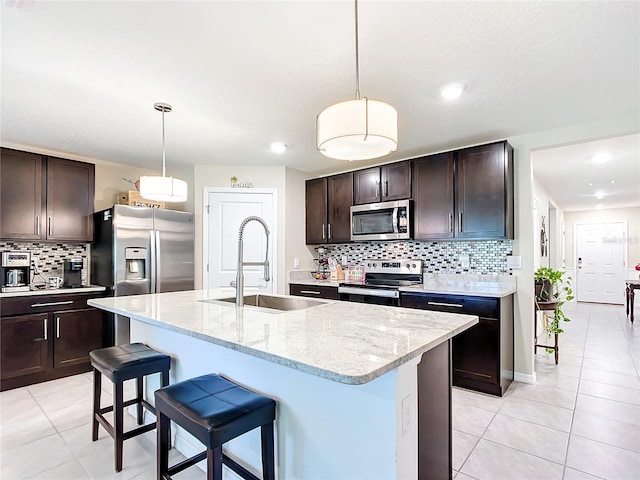 kitchen with appliances with stainless steel finishes, backsplash, pendant lighting, and a kitchen island with sink