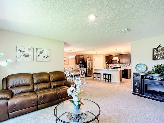 living room with light colored carpet, sink, a chandelier, and a textured ceiling