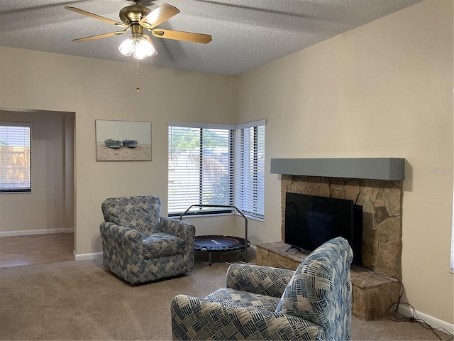 carpeted living room featuring a stone fireplace, a textured ceiling, and ceiling fan