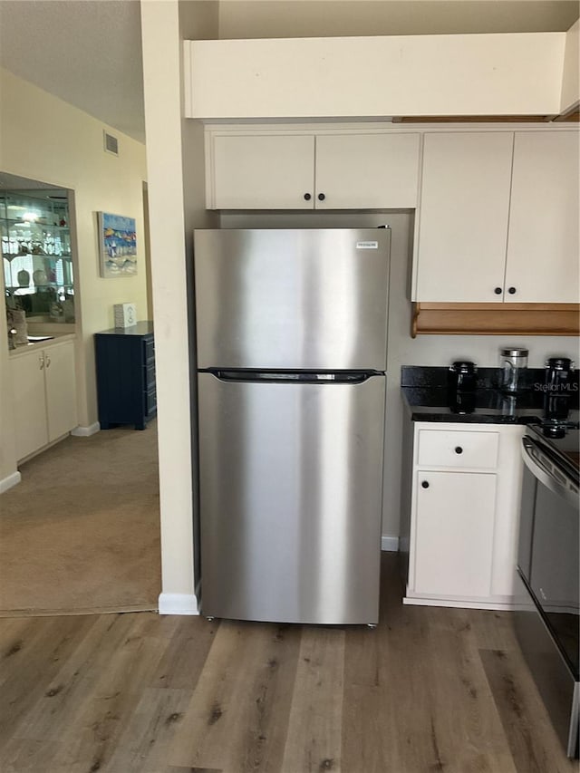 kitchen with white cabinets, light carpet, stove, and stainless steel refrigerator