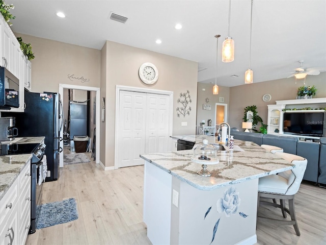 kitchen featuring white cabinetry, light hardwood / wood-style floors, electric stove, an island with sink, and light stone counters