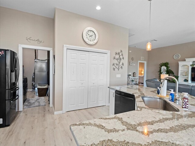 kitchen featuring light stone counters, sink, light wood-type flooring, decorative light fixtures, and black appliances