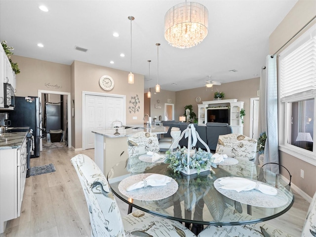 dining space with sink, ceiling fan with notable chandelier, and light wood-type flooring