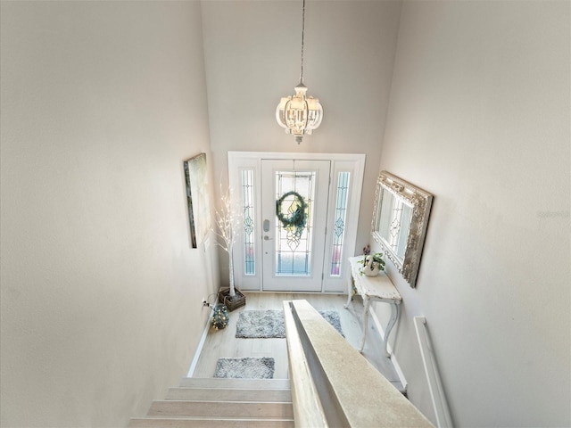 entryway with light hardwood / wood-style flooring, a towering ceiling, and a chandelier