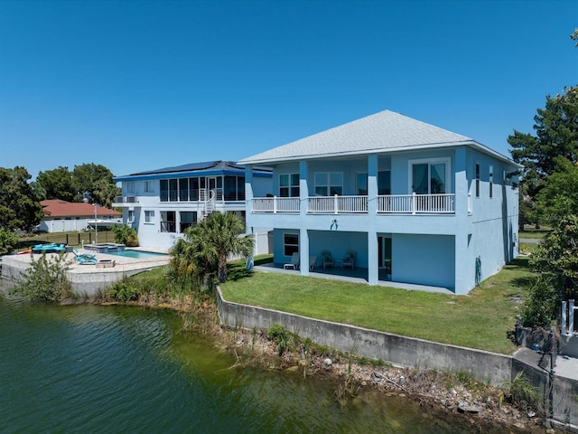 back of property featuring a water view, a balcony, a yard, and a patio area