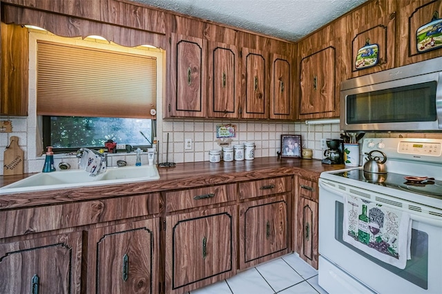 kitchen with a textured ceiling, tasteful backsplash, sink, light tile floors, and white range with electric stovetop