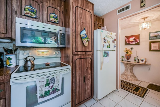 kitchen with a textured ceiling, white appliances, and light tile floors