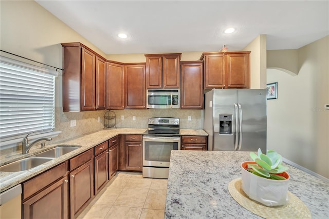 kitchen featuring appliances with stainless steel finishes, light tile flooring, tasteful backsplash, light stone counters, and sink