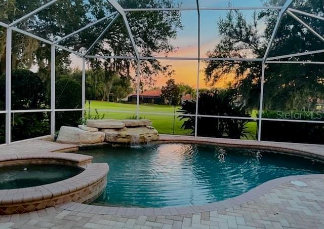 pool at dusk featuring a lanai and an in ground hot tub