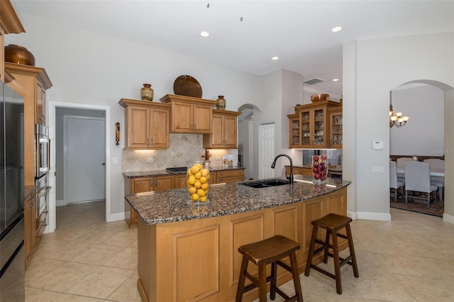 kitchen with decorative backsplash, a kitchen breakfast bar, sink, light tile patterned floors, and dark stone countertops