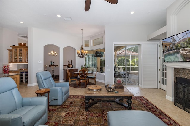 tiled living room with ceiling fan with notable chandelier and a tiled fireplace