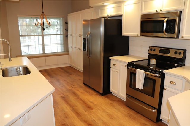 kitchen with white cabinets, appliances with stainless steel finishes, light hardwood / wood-style flooring, pendant lighting, and sink