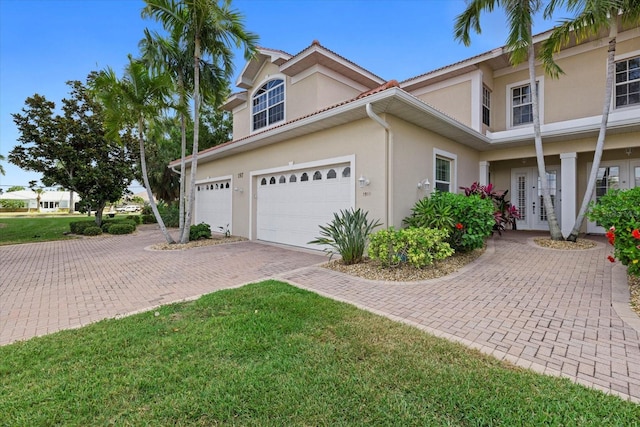 view of property exterior featuring decorative driveway, a lawn, stucco siding, and french doors