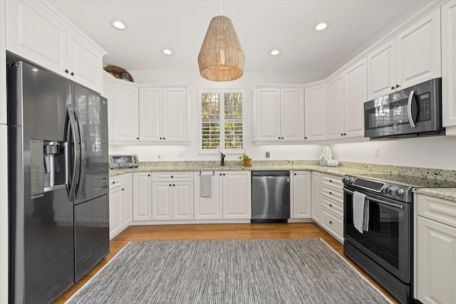 kitchen with pendant lighting, white cabinets, sink, light stone countertops, and stainless steel appliances