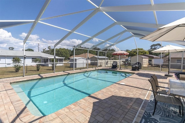 view of pool featuring glass enclosure, a storage shed, and a patio area