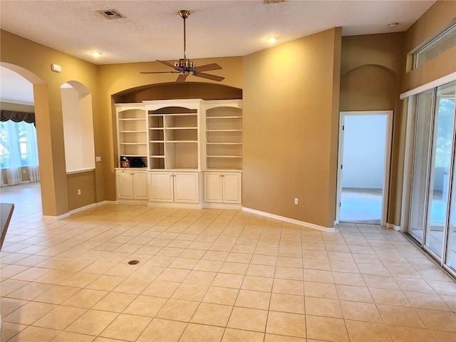 empty room featuring a textured ceiling, ceiling fan, light tile flooring, and built in shelves