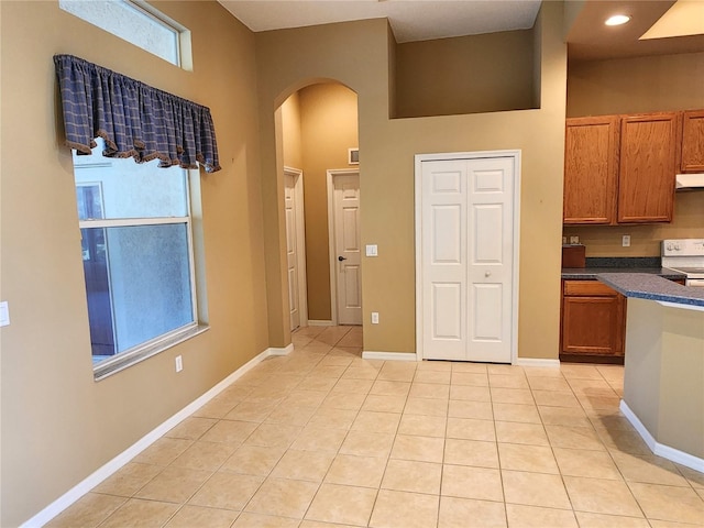 kitchen with a towering ceiling, white electric stove, and light tile floors